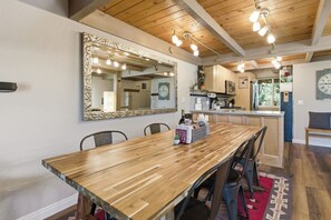 Un coin repas avec une table en bois, des chaises, un grand miroir et une cuisine en arrière-plan.