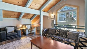 A cozy living room with a wooden ceiling, a large window with a view of buildings, a fireplace, and a sofa set. - Pet-Friendly 3BR | Heavenly & Fireplace | Sleeps 7 (Stateline)