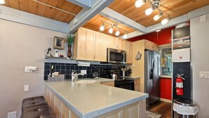 A modern kitchen with wooden cabinets, a stainless steel refrigerator, a microwave, and a large island with bar stools. - Pet-Friendly 3BR | Heavenly & Fireplace | Sleeps 7 (Stateline)