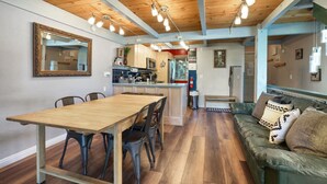 A spacious living area with a wooden dining table and chairs, a green sofa, and a kitchen in the background. - Pet-Friendly 3BR | Heavenly & Fireplace | Sleeps 7 (Stateline)