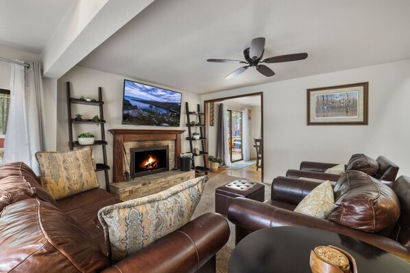 A living room with a fireplace, leather sofas, a television, and a ceiling fan.