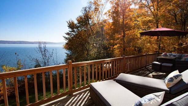 Una terraza con vista a un lago, barandas de madera y mobiliario exterior.