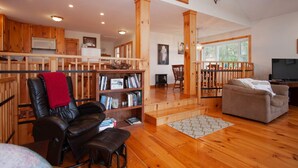 A spacious living area with wooden flooring, a leather chair, a bookshelf, and a television. - Killington Retreat | Deck-Fire Pit-Mountain Views! (Clarendon)