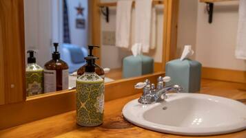 A bathroom with a wooden vanity, a white sink, a mirror, and toiletries including a patterned bottle and a pump bottle.