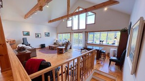 A spacious living area with a wooden staircase, a dining area, and large windows providing natural light. - Killington Retreat | Deck-Fire Pit-Mountain Views! (Clarendon)
