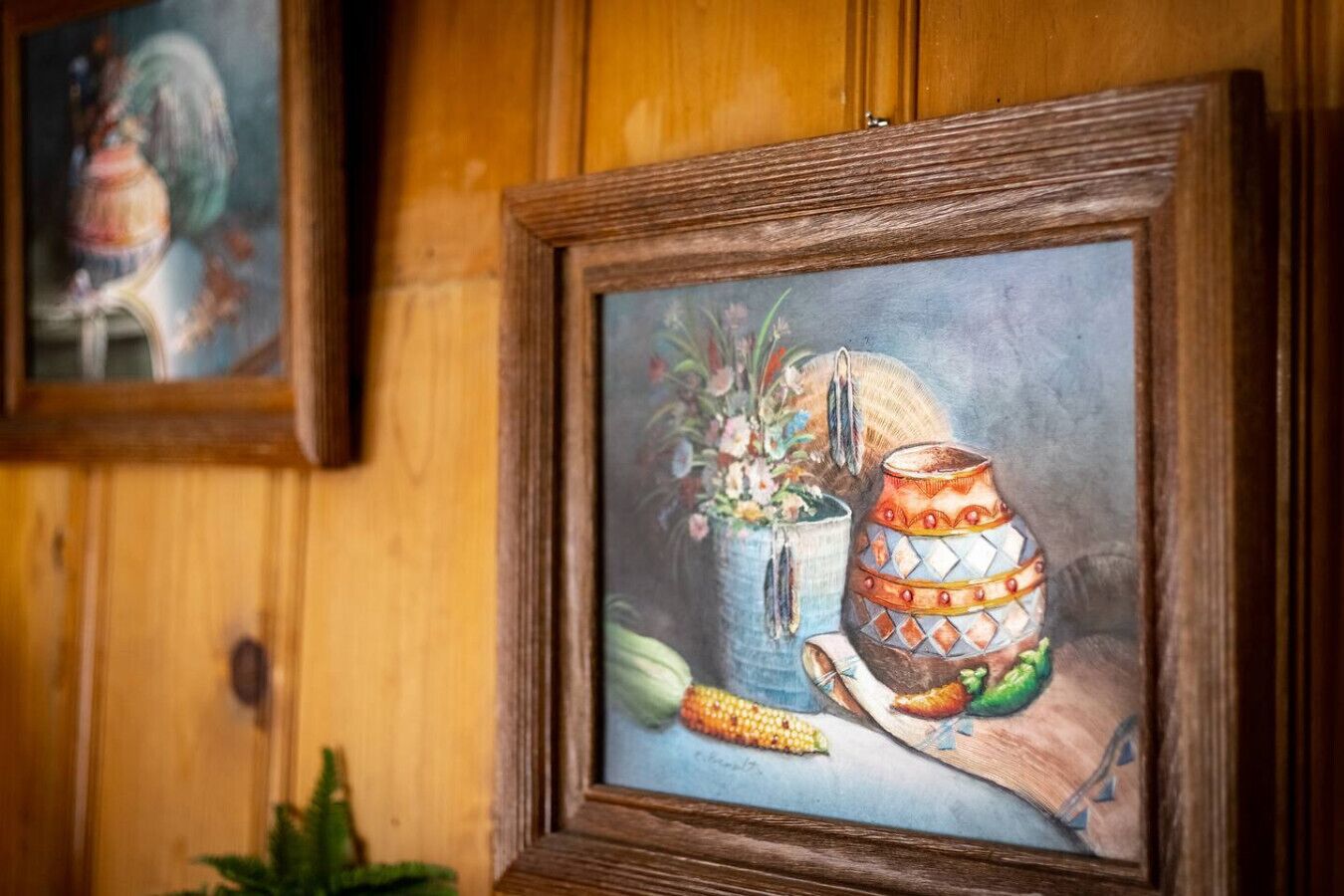 Een lijst met een schilderij van een stilleven met keramiek en mais op een houten oppervlak.