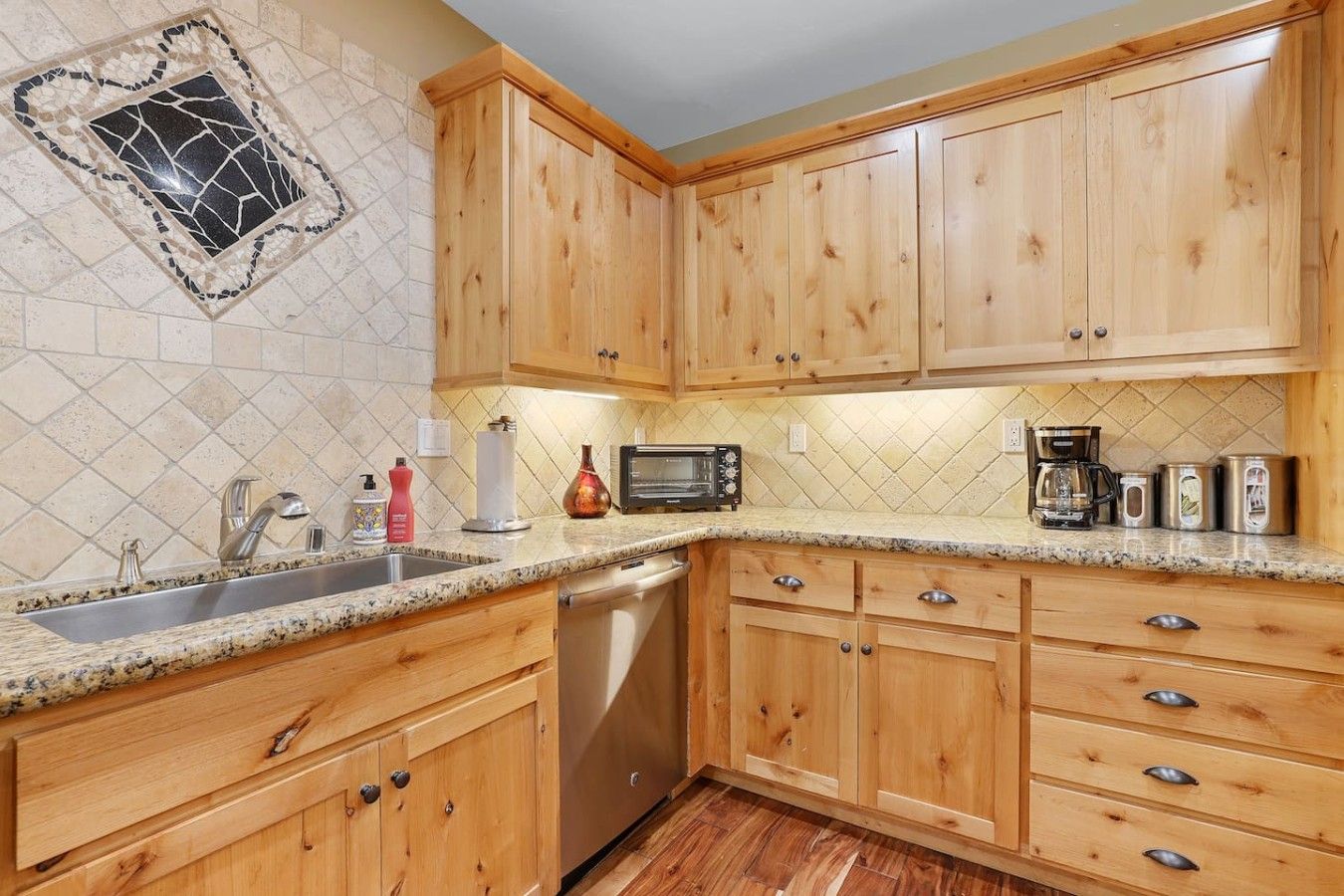 A kitchen with wooden cabinets, a stainless steel dishwasher, and a granite countertop.