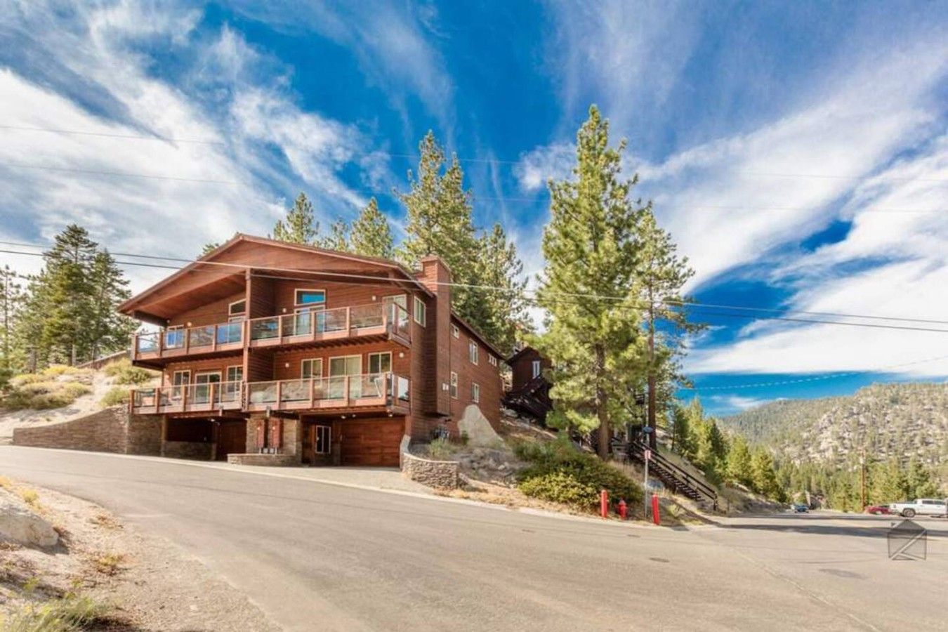 A two-story wooden cabin with a balcony, surrounded by trees and a clear sky.
