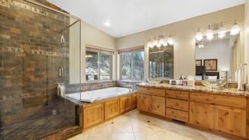 A spacious bathroom with a large shower, a freestanding bathtub, wooden cabinetry, and a vanity with a large mirror and lights.