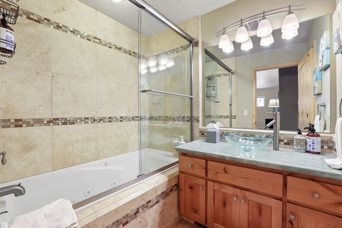 A bathroom with a glass-enclosed shower, a bathtub, a vanity with a glass bowl sink, and a large mirror.
