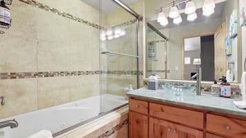 A bathroom with a glass-enclosed shower, a bathtub, a vanity with a glass bowl sink, and a large mirror.