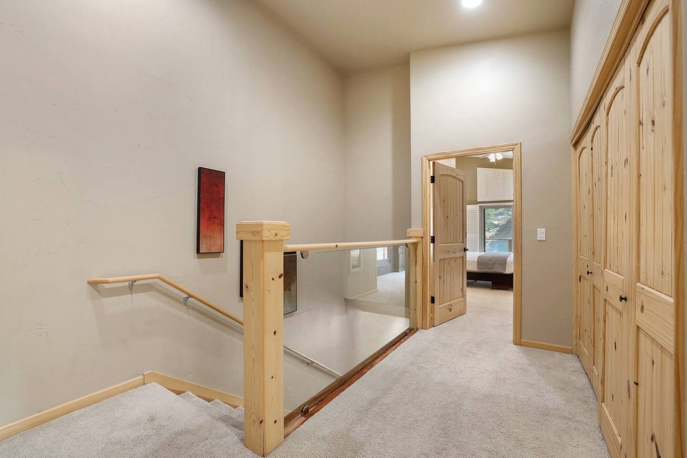 A staircase with wooden handrails and a glass balustrade leading to a bedroom with a bed and a window.