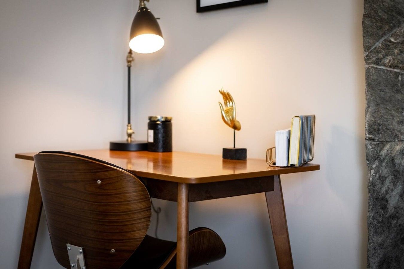 A wooden desk with a lamp, a decorative sculpture, and books.