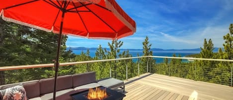 A deck with a fire pit, outdoor seating, and a red umbrella.