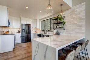 A modern kitchen with white cabinetry, a central island, stainless steel appliances, and pendant lighting.