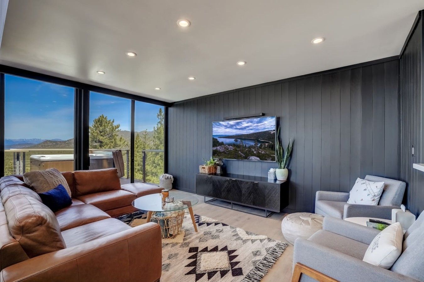 A modern living room with a large window, leather sofas, a flat-screen TV, and a decorative rug.