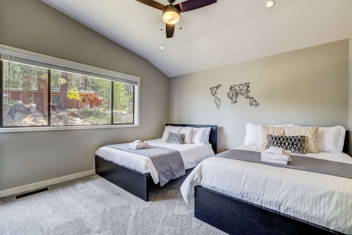 A bedroom with two beds, a ceiling fan, and a large window with a view of trees and a building.