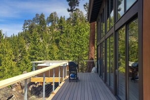 A wooden deck with a barbecue grill, overlooking a forested area.