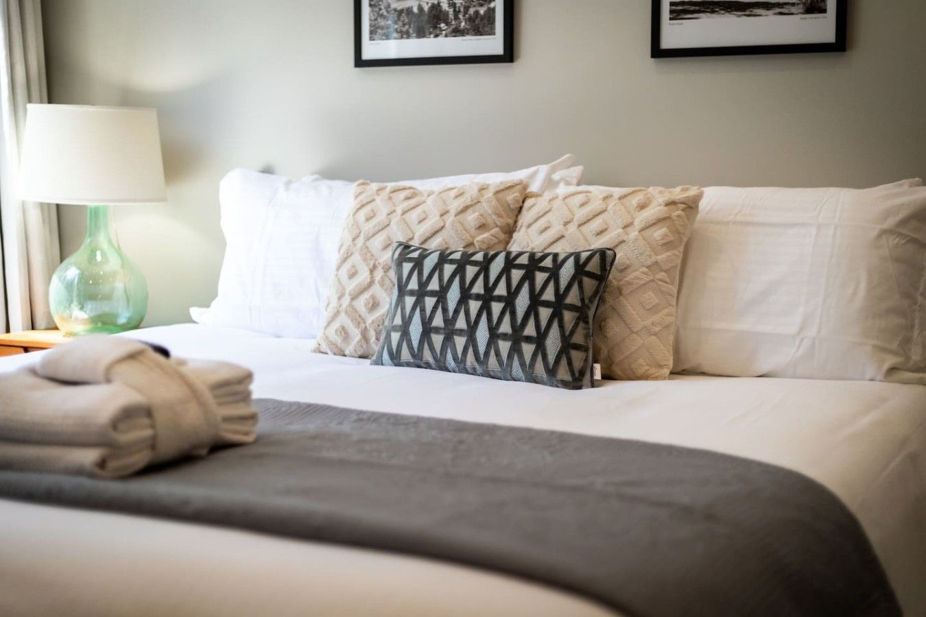 A neatly made bed with a grey blanket, two patterned pillows, and a folded towel on the side.