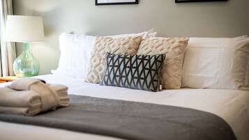 A neatly made bed with a grey blanket, two patterned pillows, and a folded towel on the side.