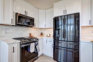 A modern kitchen with white cabinetry, a stainless steel refrigerator, a built-in oven, and a microwave.