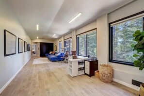 A modern interior with a long hallway, a blue sofa, a desk, and large windows.