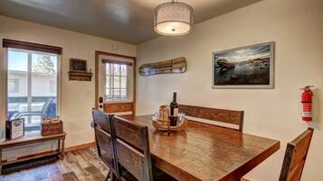 A dining area with a wooden table, chairs, a hanging light fixture, a framed picture, and a fire extinguisher.