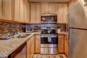 A compact kitchen with wooden cabinets, a stainless steel refrigerator, a microwave, a stove, and a sink. - Cozy Condo | Near Heavenly-Fireplace | Sleeps 6 (Stateline)