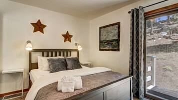 A bedroom with a bed, two wall-mounted star decorations, a painting, and a view of a rocky landscape through a window.