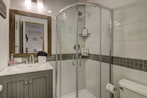 Een badkamer met een douchecabine van glas, een wastafel met spiegel erboven en een handdoekrek.