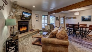 A cozy living room with a fireplace, a stone accent wall, and a dining area with a wooden table and chairs. - Cozy Condo | Near Heavenly-Fireplace | Sleeps 6 (Stateline)