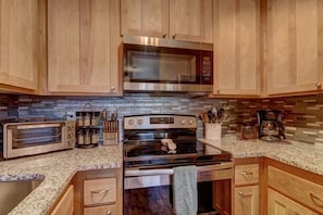 A kitchen with wooden cabinets, a microwave, a toaster oven, and a stove.
