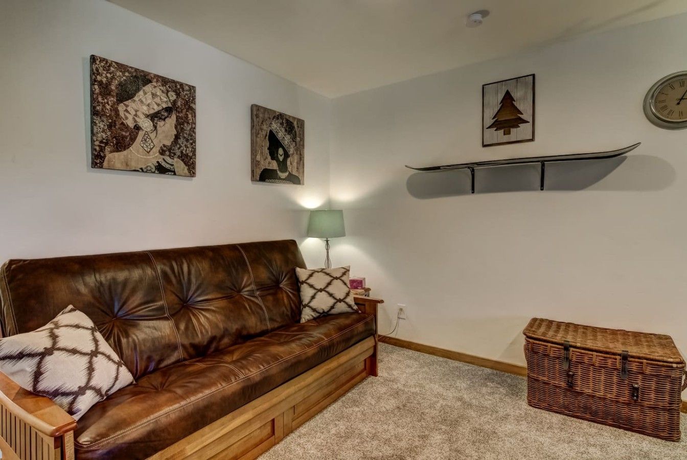 Een woonkamer met een bruine leren bank, een groene vloerlamp en een rieten dressoir.