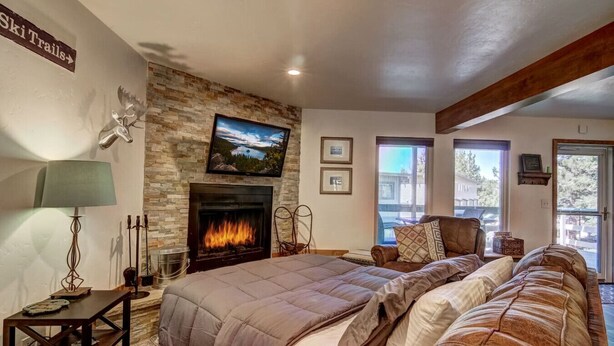 A cozy bedroom with a stone fireplace, a bed with a large comforter, a mounted TV, and a sign indicating 'Ski Trails'. - Cozy Condo | Near Heavenly-Fireplace | Sleeps 6 (Stateline)