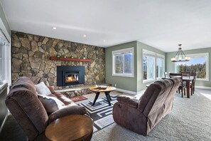 A living room with a stone wall, fireplace, leather sofas, and a dining area with a view.