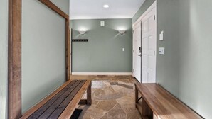 Un couloir avec un sol en pierre, des bancs en bois, un porte-manteau et une porte dotée d’un interrupteur.