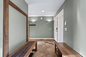 Un couloir avec un sol en pierre, des bancs en bois, un porte-manteau et une porte dotée d’un interrupteur.