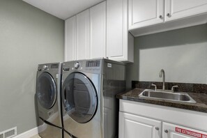 A laundry room with two front-loading washing machines, a stainless steel sink, and white cabinets. - Luxury 4BR | BBQ, Hot Tub & Lake Views | Sleeps 8 (Glenbrook)