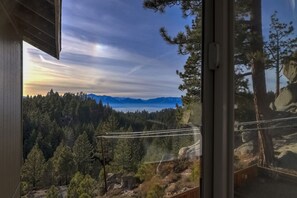 Une vue depuis une fenêtre donnant sur un paysage montagneux boisé, avec un ciel dégagé.
