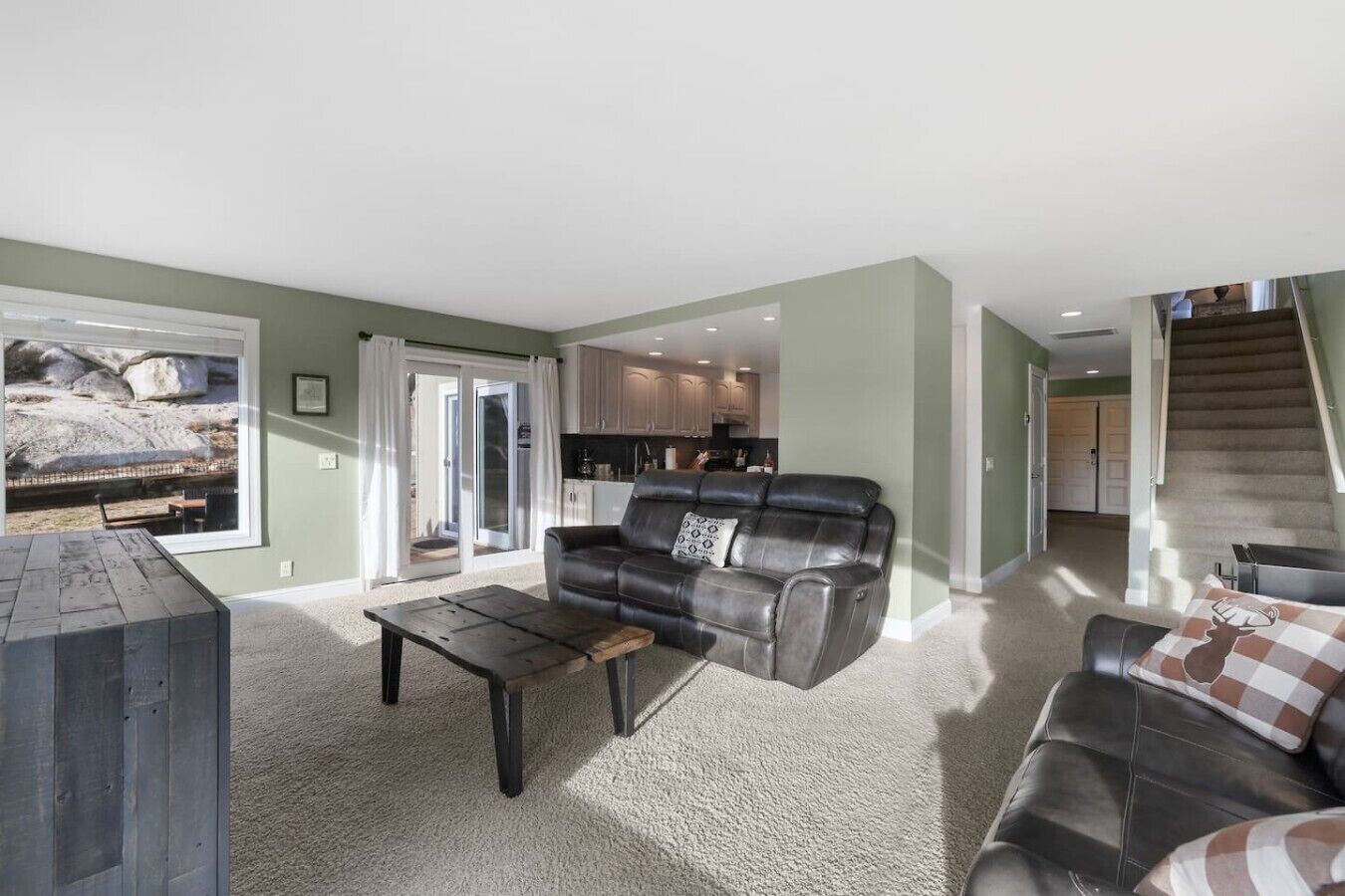 A living room with a sofa, a coffee table, and a view of a kitchen and a staircase.
