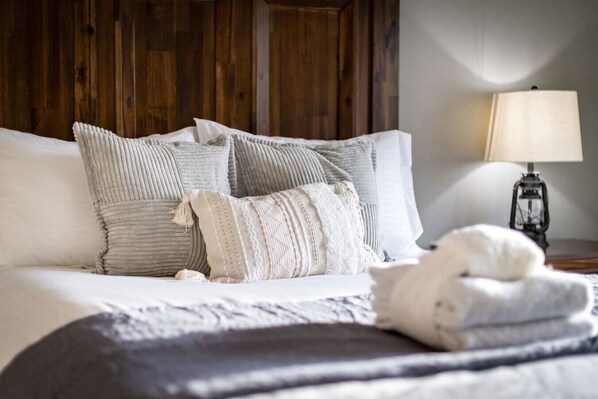 A bed with multiple pillows and a blanket, a lamp on a bedside table, and a wooden headboard.