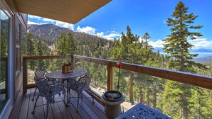 A wooden deck with a table and chairs, overlooking a forested mountain landscape. - Heavenly Escape | Lake Views, Pets OK | Sleeps 6 (Stateline)