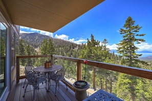 A wooden deck with a table and chairs, overlooking a forested mountain landscape. - Heavenly Escape | Lake Views, Pets OK | Sleeps 6 (Stateline)