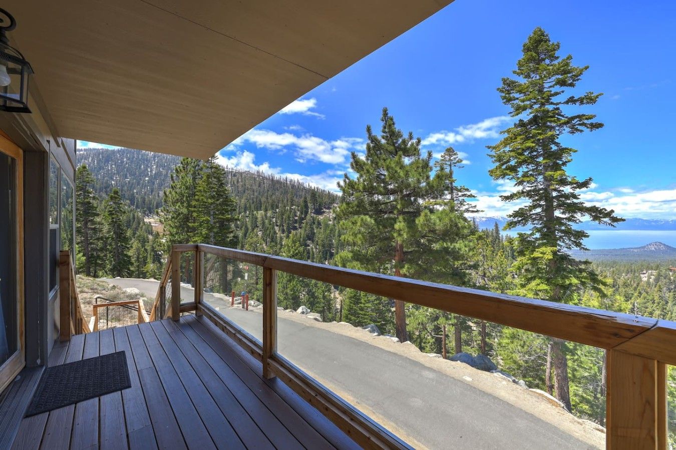 Eine Holzdielen-Terrasse mit Metallgeländer, mit Blick auf einen bewaldeten Bereich und eine Straße.