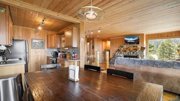 A wooden cabin interior with a dining area, kitchen, and a stone fireplace.