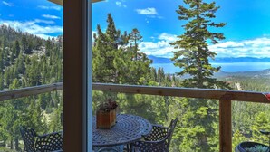 A balcony with a table and chairs, overlooking a forested landscape and a lake. - Heavenly Escape | Lake Views, Pets OK | Sleeps 7 (Stateline)