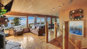 A spacious living area with a wooden ceiling, large windows offering scenic views, a cozy seating area with a sofa and chairs, and a dining area with a table and chairs. - Heavenly Escape | Lake Views, Pets OK | Sleeps 7 (Stateline)