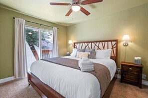 A bedroom with a bed, a nightstand, a lamp, a ceiling fan, and a view of the outdoors through a window. - Ski-In Heavenly Condo | Cozy 3BR | Sleeps 8 (Stateline)