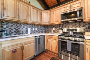 A kitchen with wooden cabinets, a stainless steel stove, a microwave, and a tiled backsplash. - Ski-In Heavenly Condo | Cozy 3BR | Sleeps 8 (Stateline)
