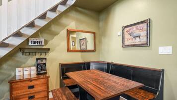 A corner seating area with a wooden table and benches, a coffee station with labeled containers, and a framed picture on the wall.